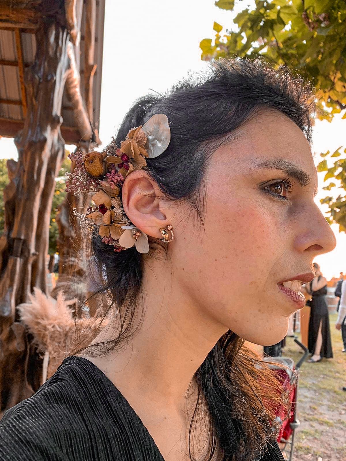 Ear adornment of dried florals and shell worn at an outdoor celebration